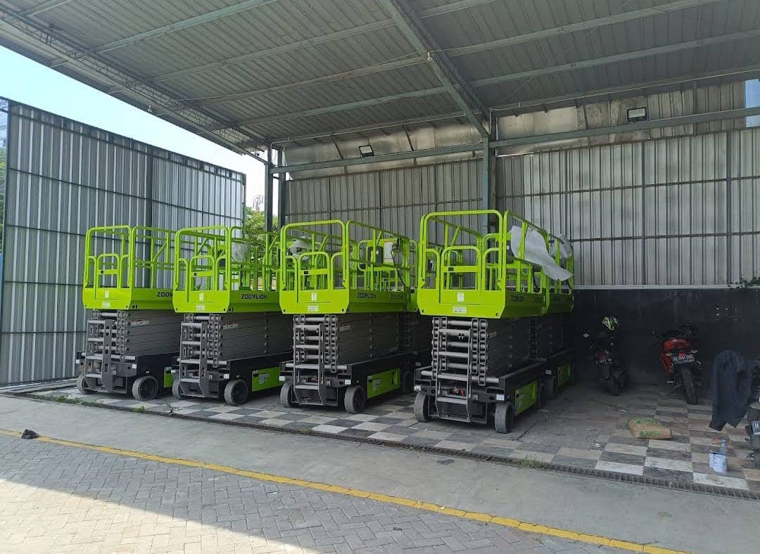 Empat unit scissor lift Zoomlion hijau terparkir rapi di bawah naungan atap gudang industri.