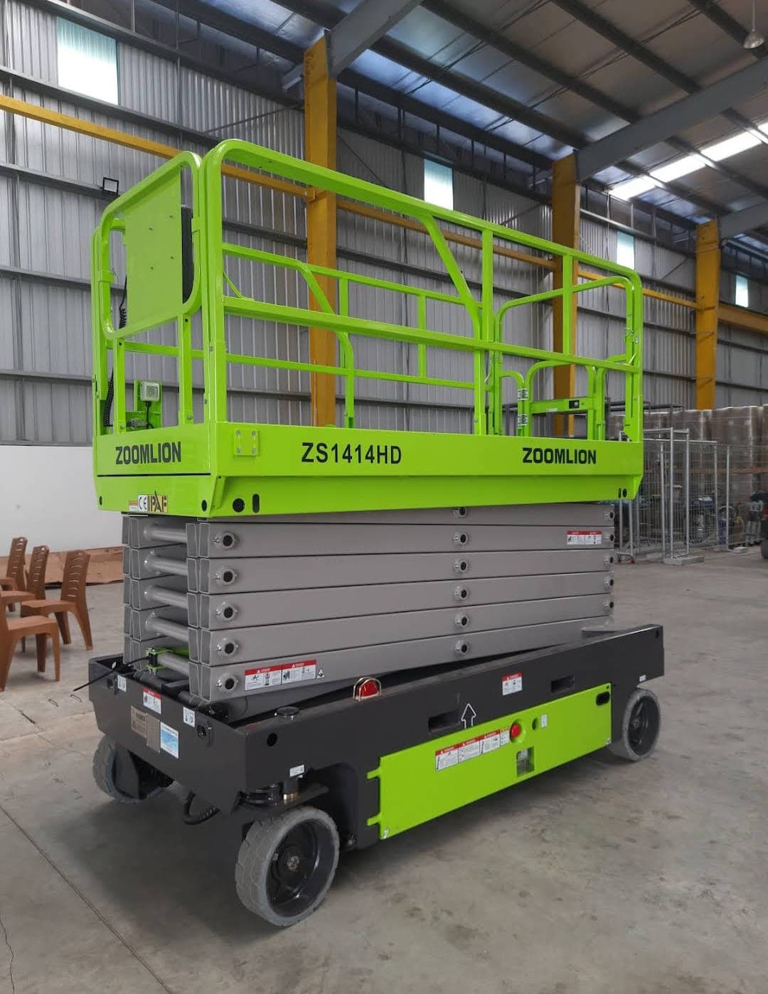 Lift gunting Zoomlion ZS1414HD berwarna hijau cerah terparkir di dalam sebuah gudang industri besar.