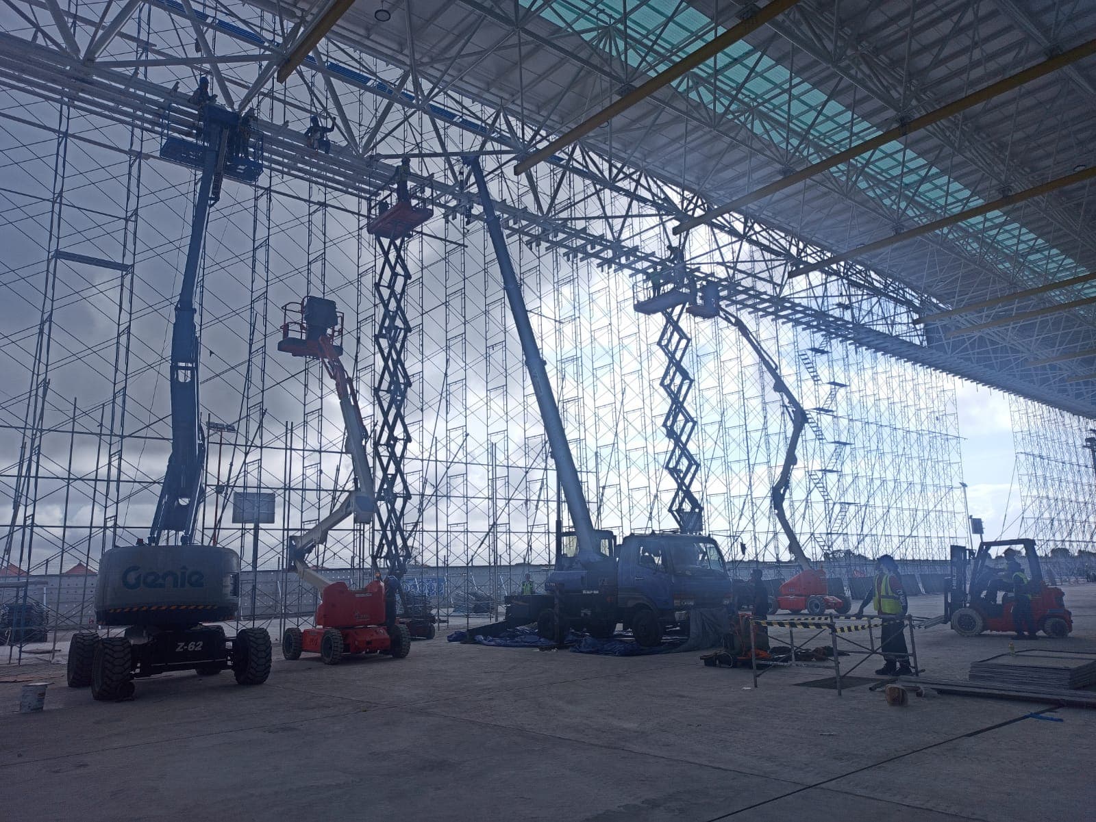 Pekerja menggunakan lift udara dan perancah untuk memasang struktur atap logam pada proyek konstruksi besar.
