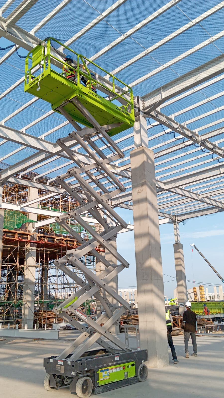 Pekerja menggunakan scissor lift untuk menjangkau struktur atap baja pada lokasi proyek konstruksi bangunan.